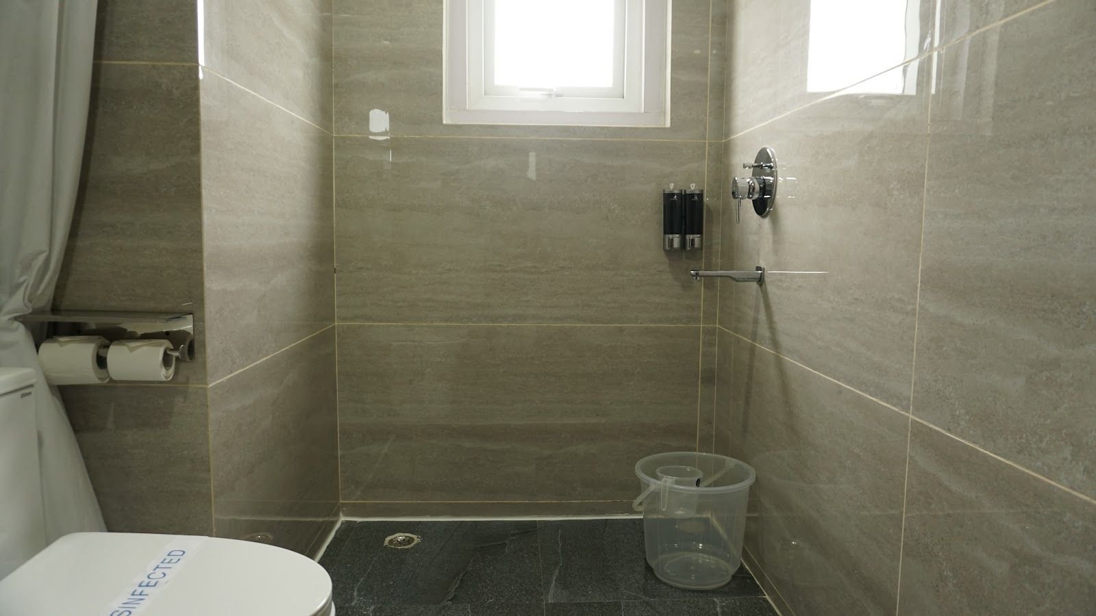 A grey-tiled bathroom with a toilet and a small frosted window