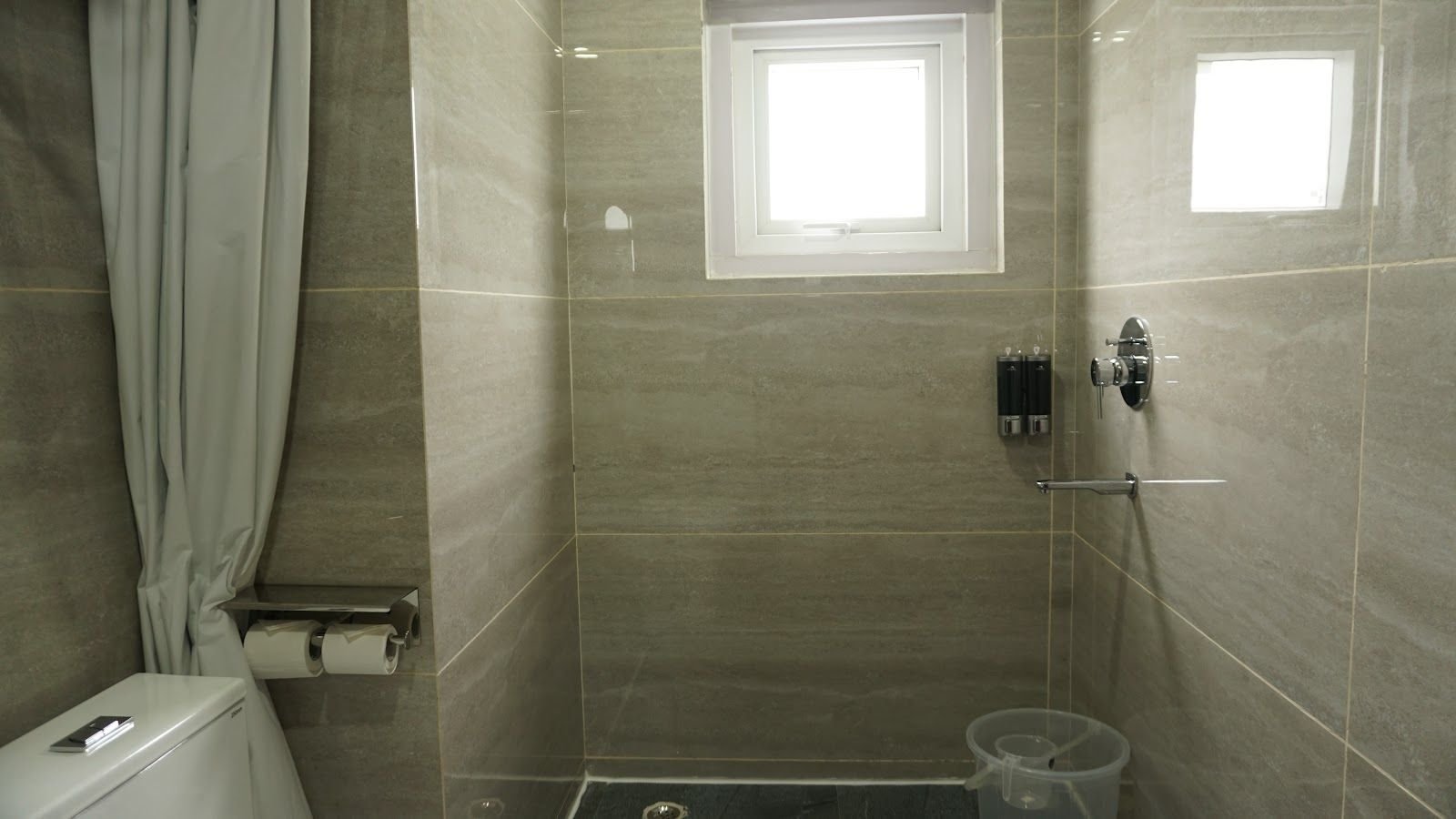 A tiled shower area with a curtain rail and a window above