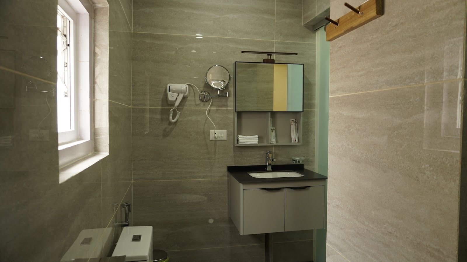 A bathroom vanity with a mirror, folded towels and a wall-mounted hairdryer