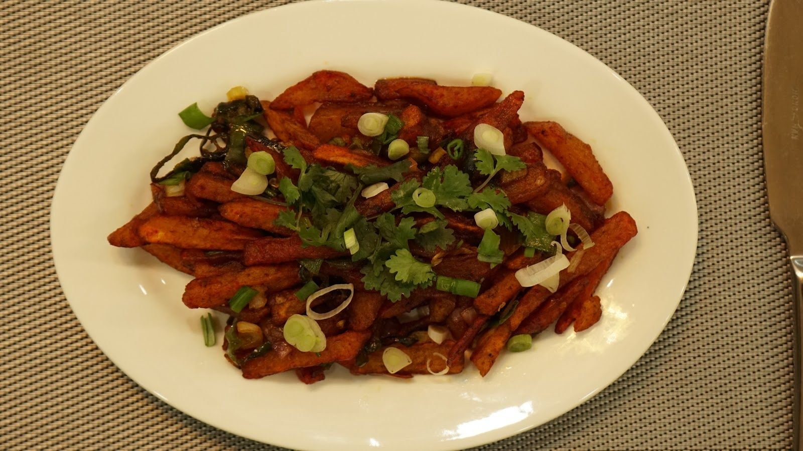 Chilli chicken in a dark red glaze, scattered with sliced spring onion