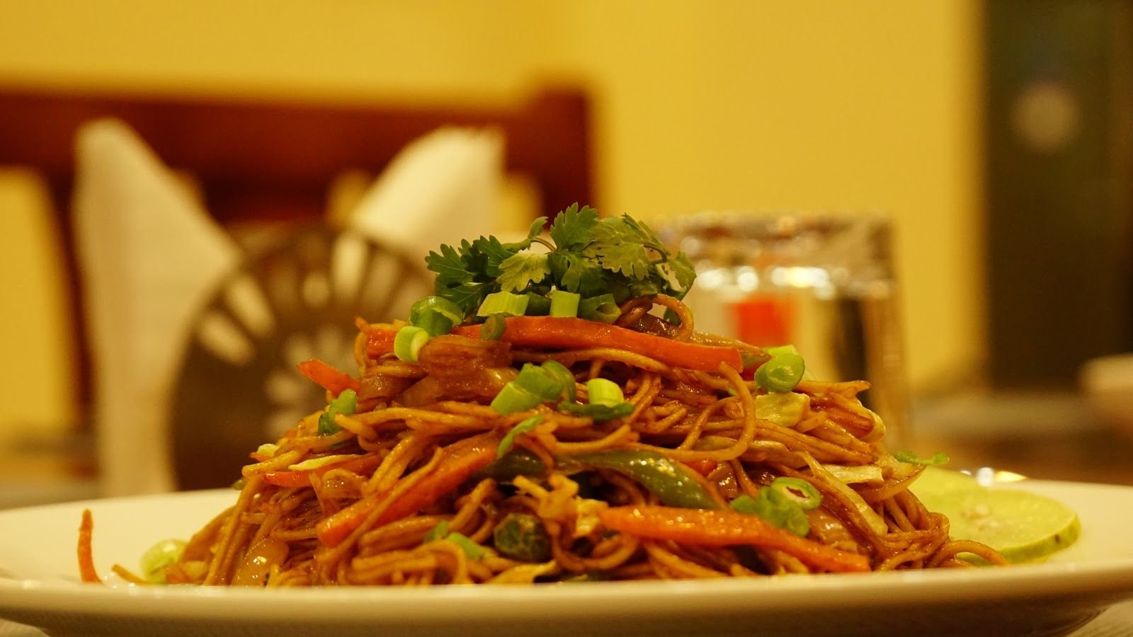 Fried noodles heaped on a white plate, photographed across the table