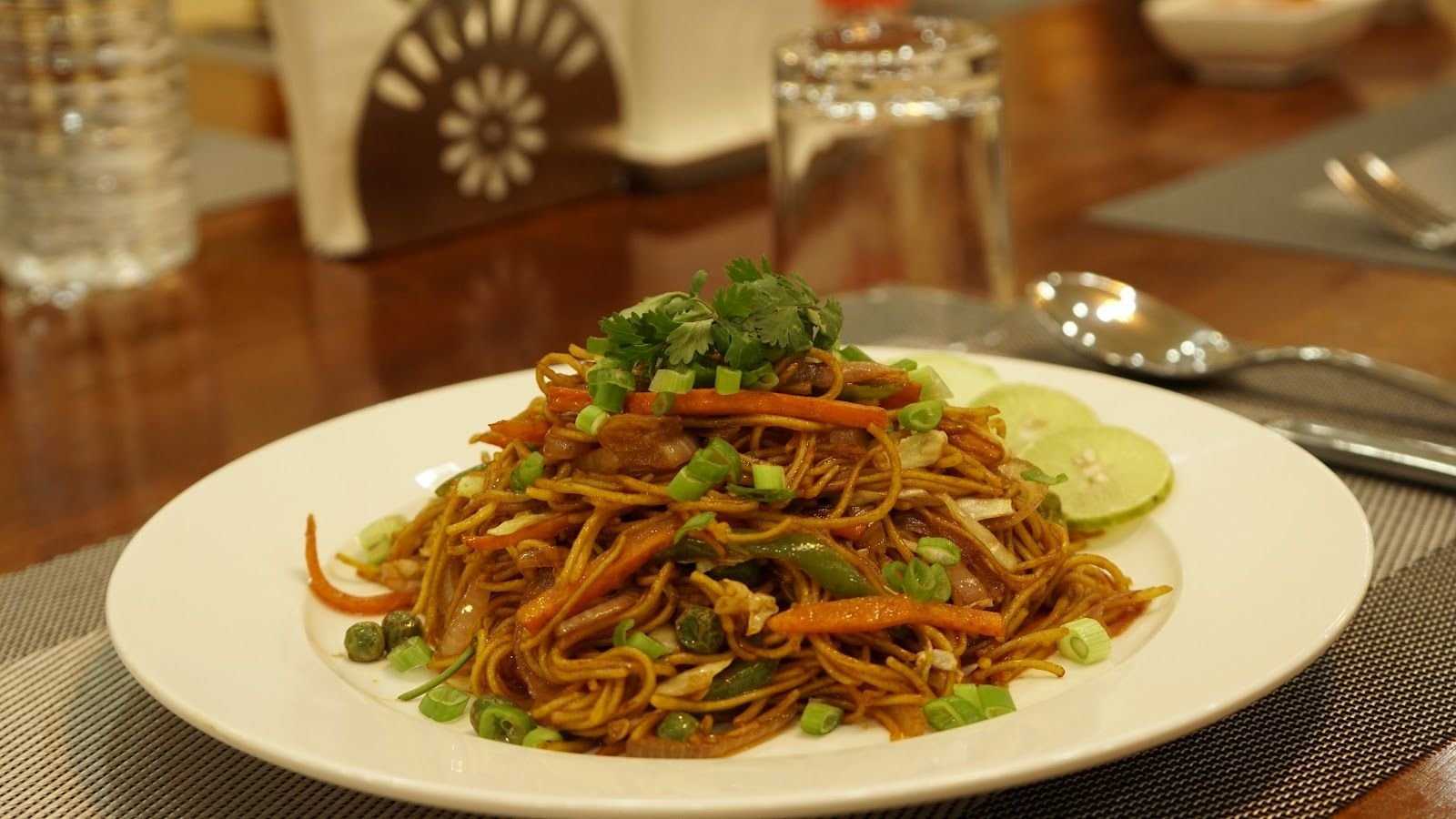 A plate of fried noodles tossed with vegetables and finished with coriander and lime