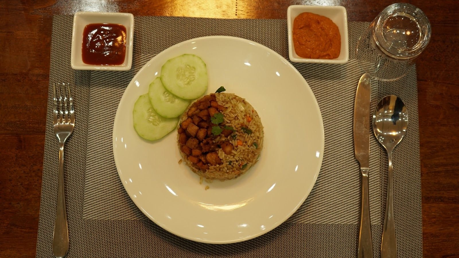 Fried rice plated with cucumber, cutlery and two small pots of chilli sauce alongside