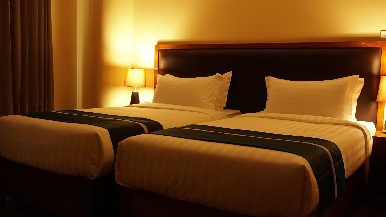 A large bed under warm lamplight, dressed in white with a dark runner