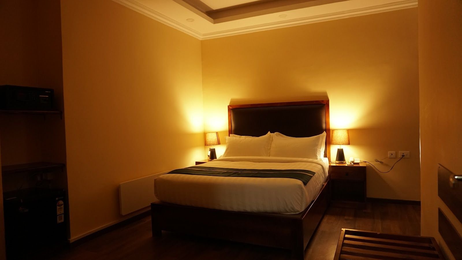 A guest room in warm amber light, bed made up beneath a tall headboard