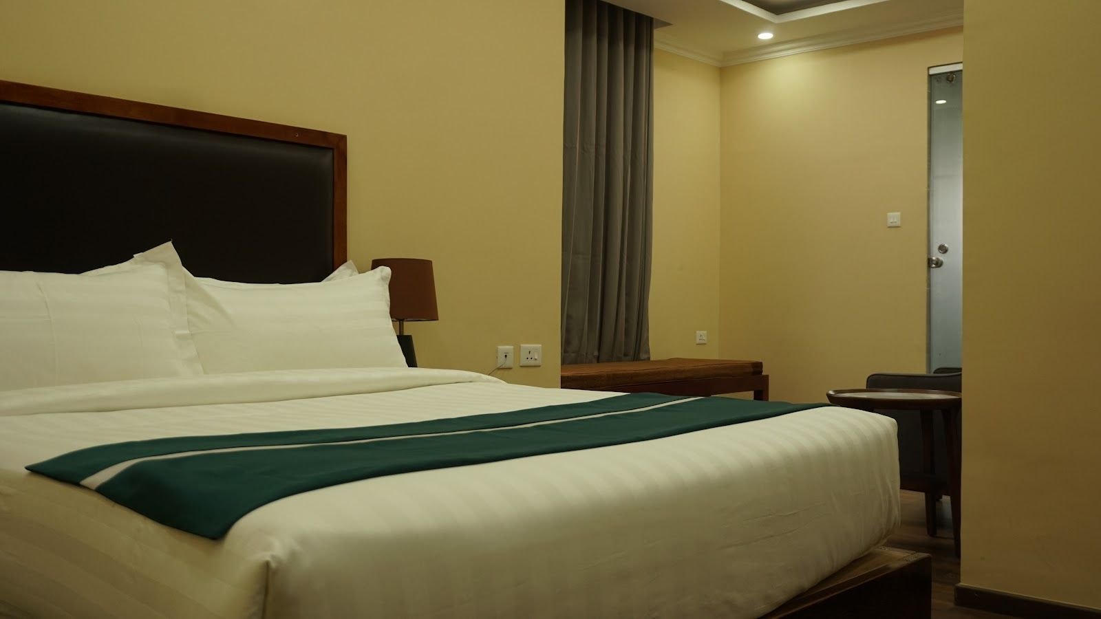 A double bed with a dark padded headboard, white linen and a teal runner