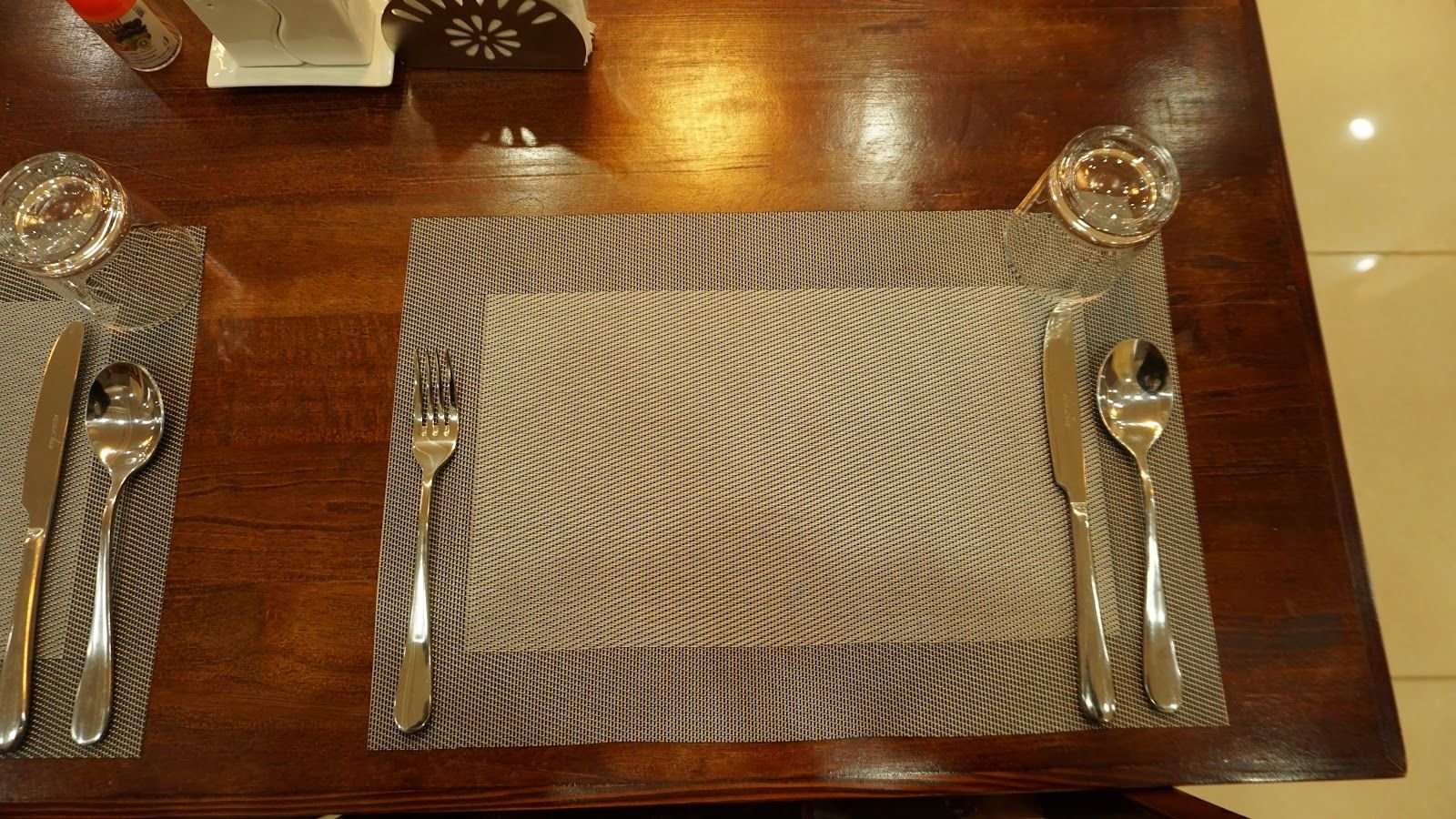 A single place setting on a polished wooden table: mat, cutlery and glass