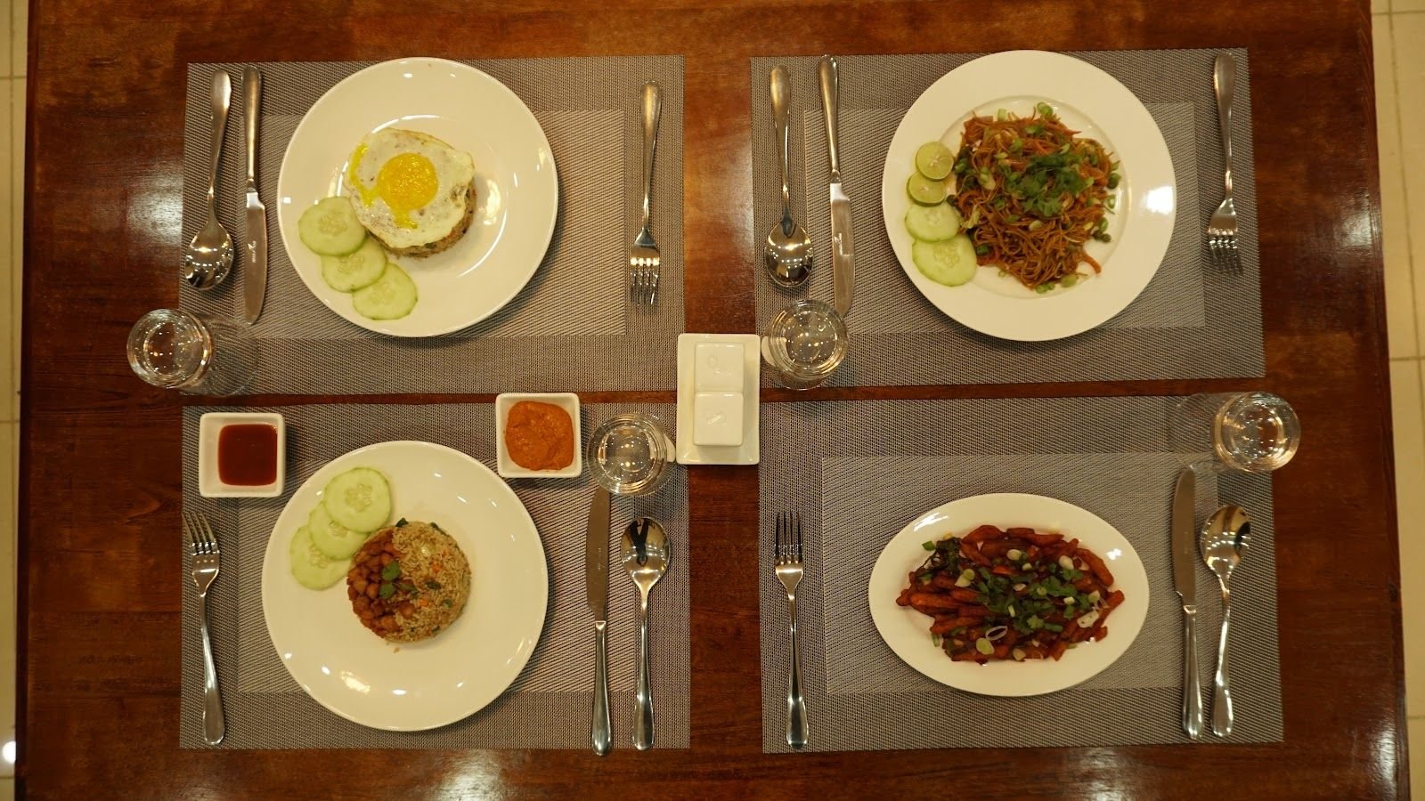 Four places laid, each with a plated dish and small dishes of chilli sauce