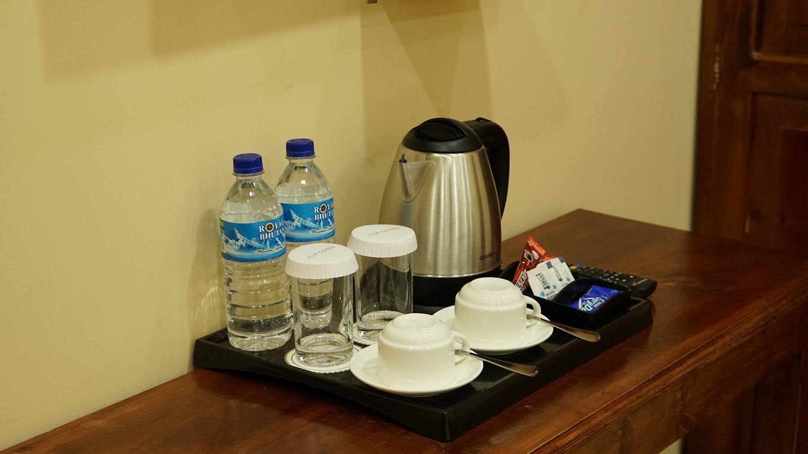 A tray on the desk with an electric kettle, cups and saucers, glasses and bottled water